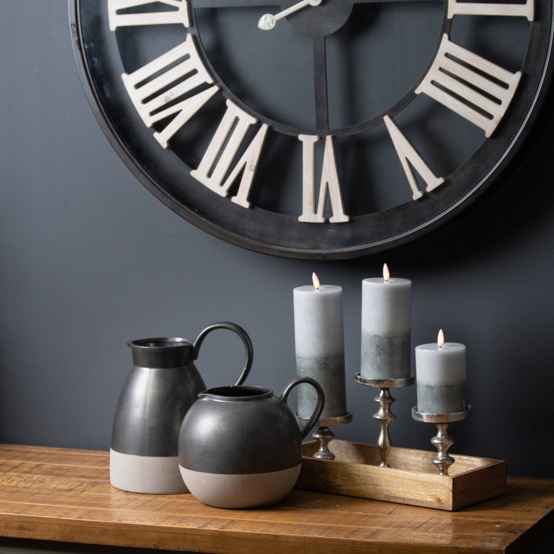 three two tone grey candles next to 2 two tone grey decorative jugs with skeleton clock to the background