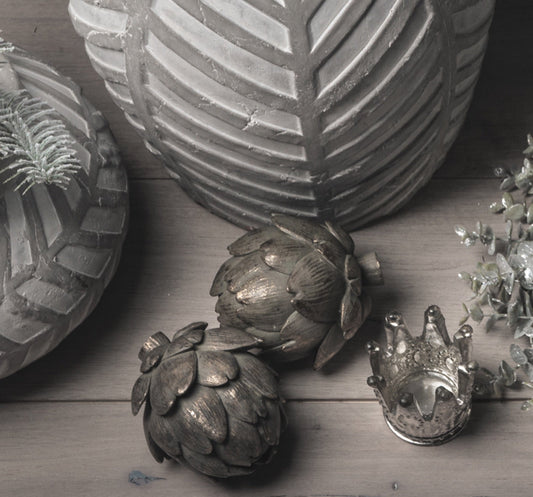 two artichokes photographed from above, next to two grey stone vases and a small crown tea light holder