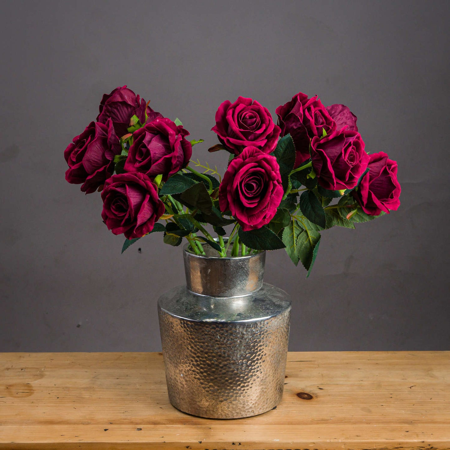 several stems of deep red rose in silver vase on wooden table