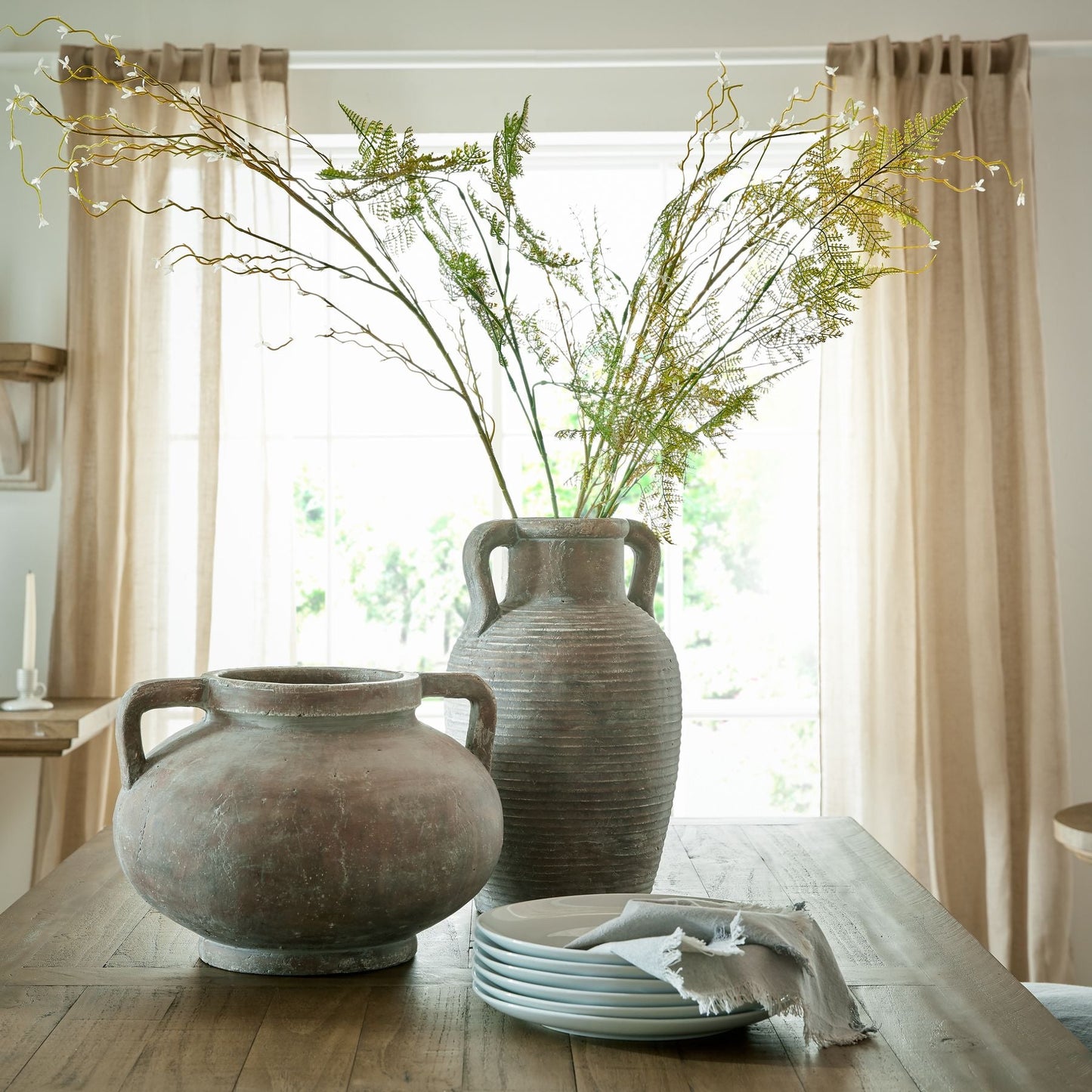 large amphora vase with artificial branches, next to small amphora style pot