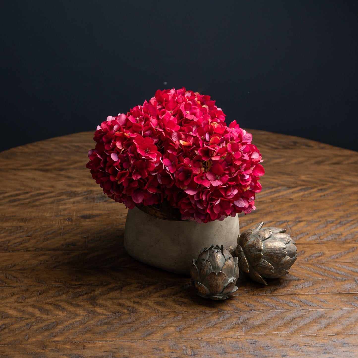 hydrangea's cut short and in short stone vase with two bronze artichokes in front