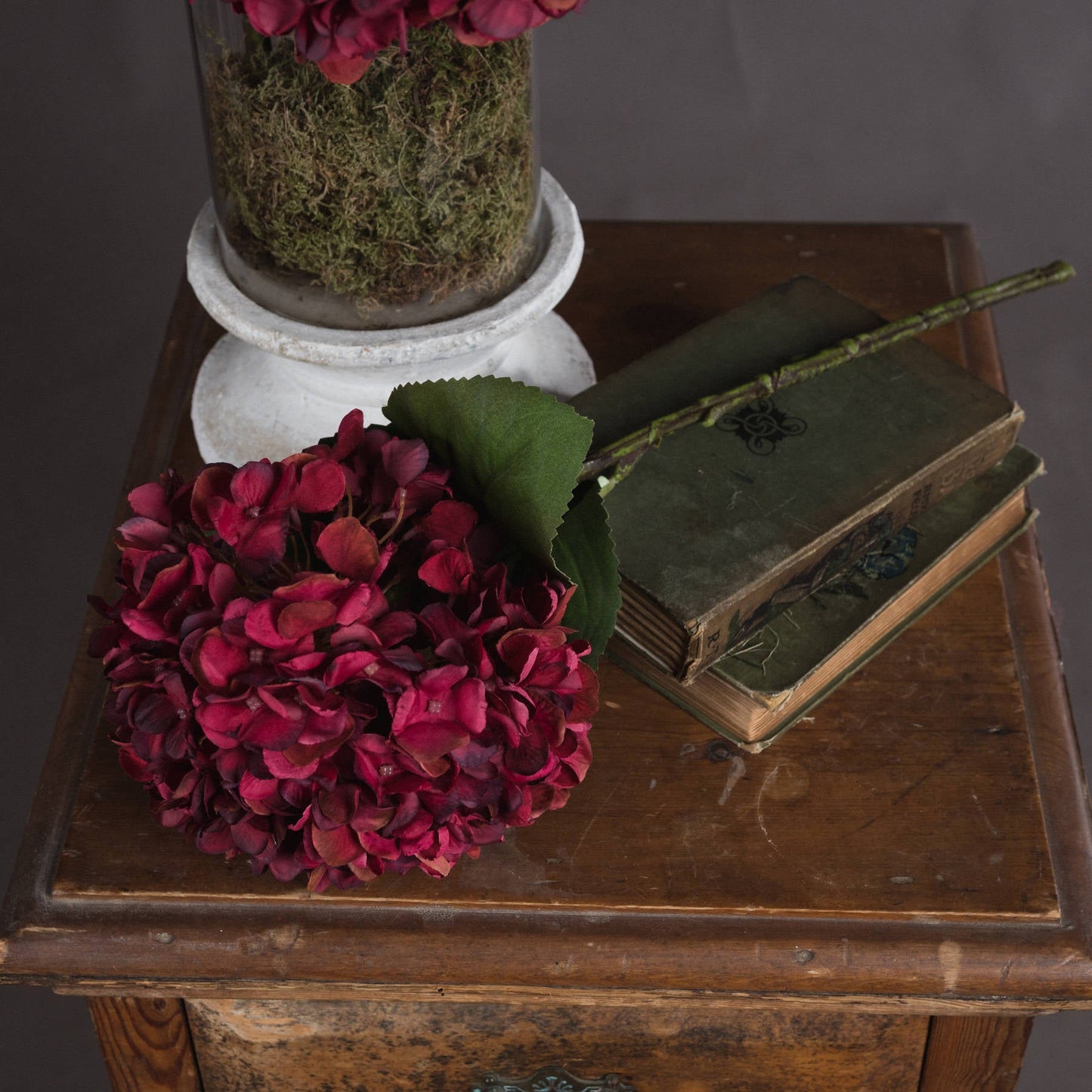 single stem ruby hydrangea laid down on side table on top of antique books