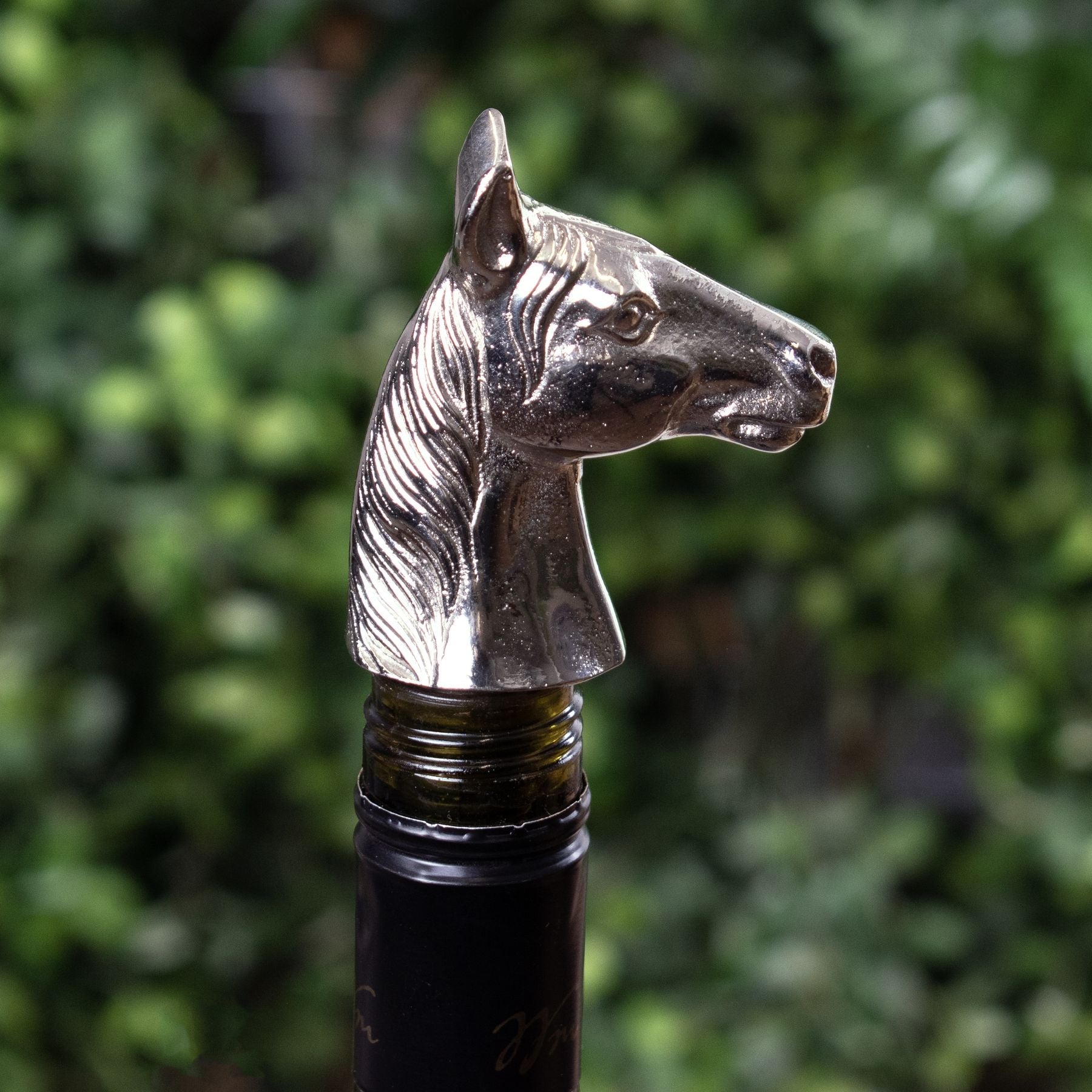 Silver nickel horse head bottle stopper in bottle of wine, out of focus greenery can be seen as the background