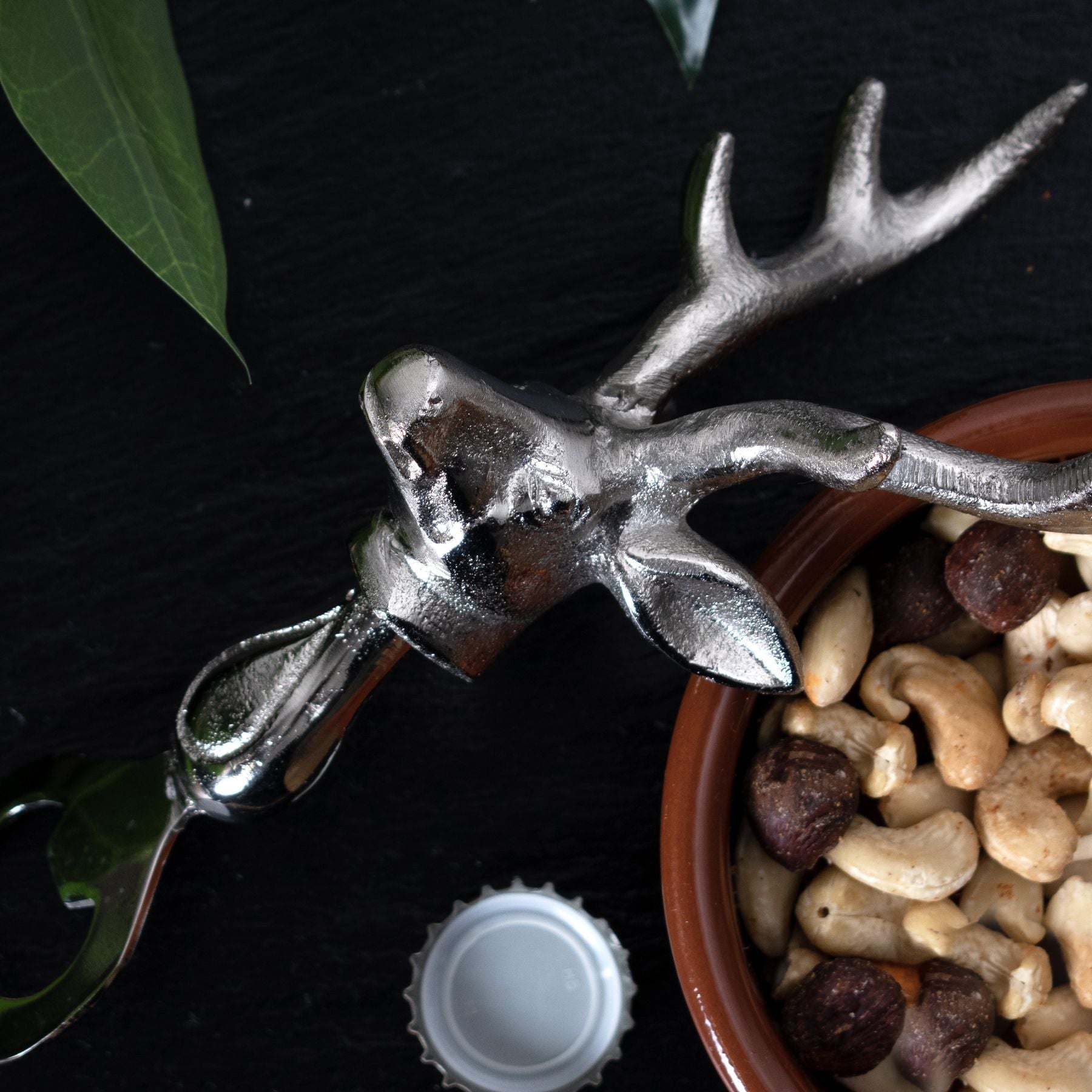 silver nickel stag head bottle opener laid on it's side of bowl of mixed nuts