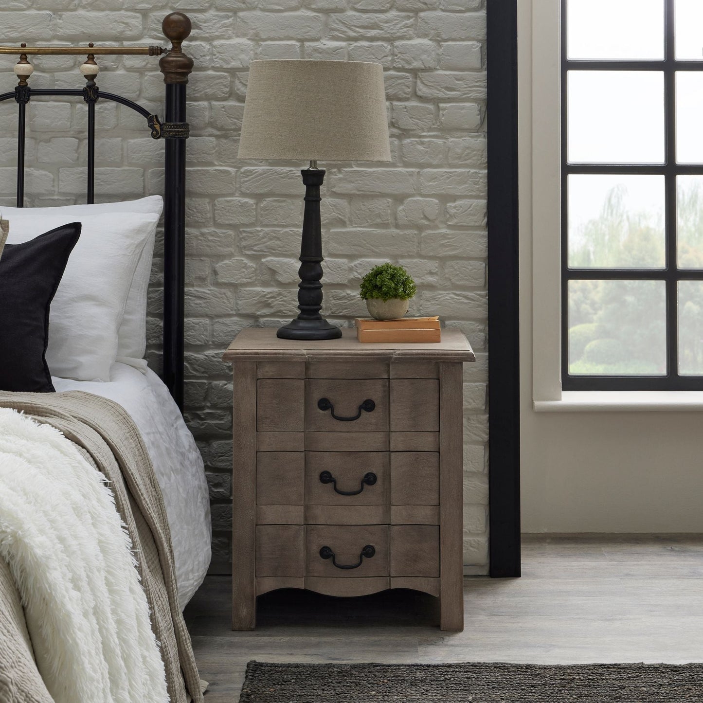 bedside next to bed, with lamp on top and small artificial hebe plant