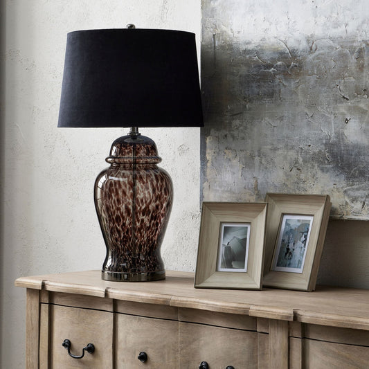 Aster black dapple lamp with black velvet shade, on sideboard next to 4x6 and 5x7 wooden photo frames. An abstract piece of grey artwork is on the wall behind