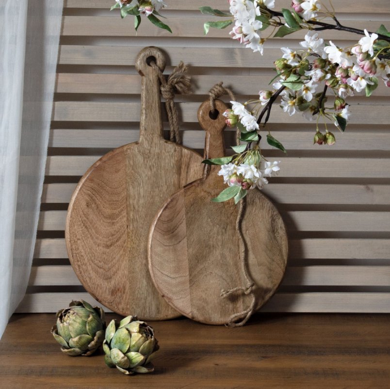 two artichokes in front of a small and large round chopping board