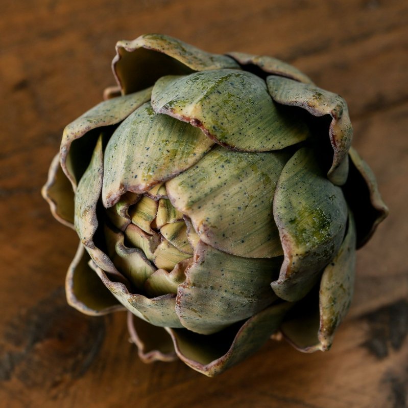 realistic artificial artichoke shown on wooden top