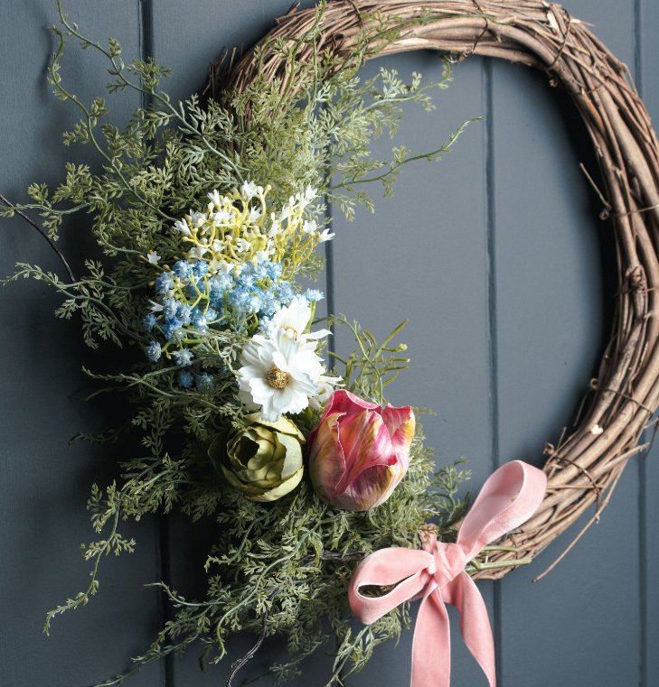 asparagus fern bunch as part of spring wreath, wreath is made of rattan, with faux florals on and pink velvet bow to the bottom