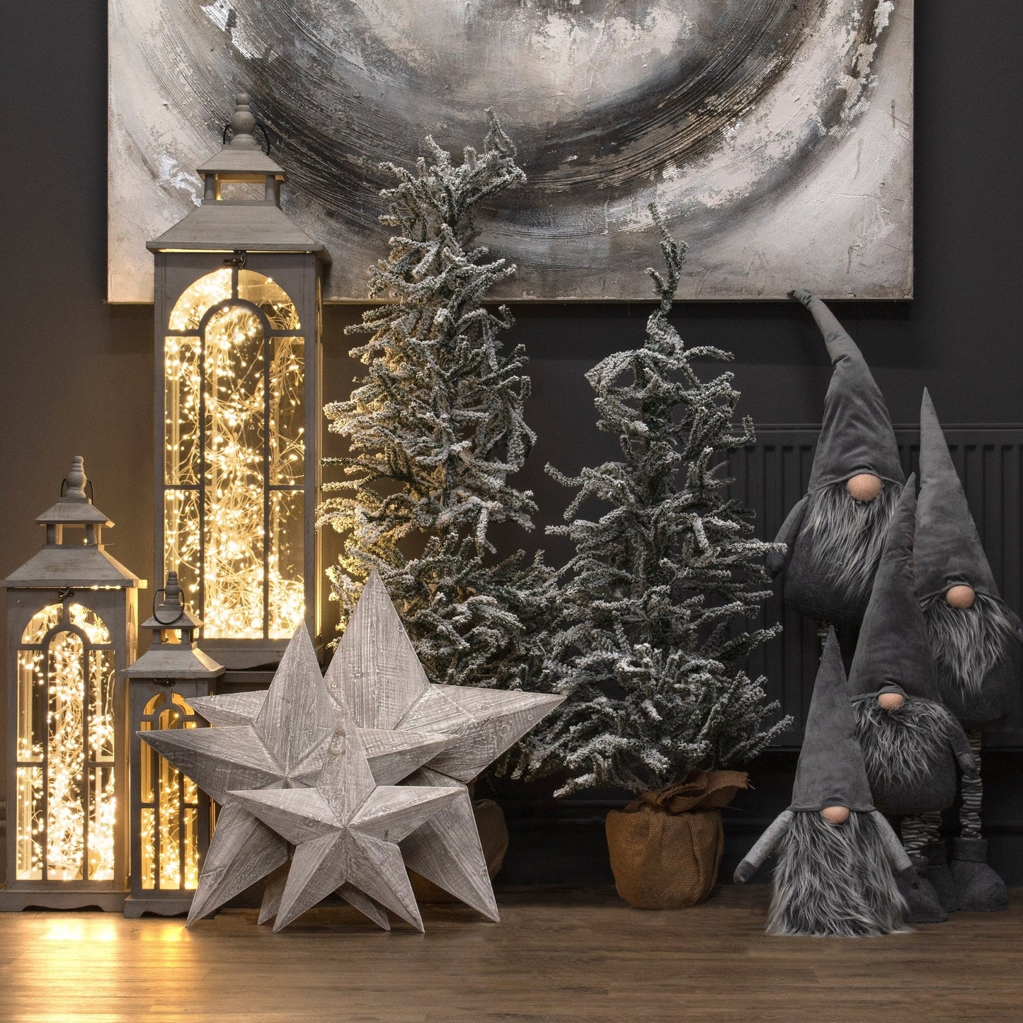 lifestyle image of the three lanterns on the left, next to three grey stars, two christmas trees and four varying size gonks. A grey piece of artwork is mounted to the wall behind