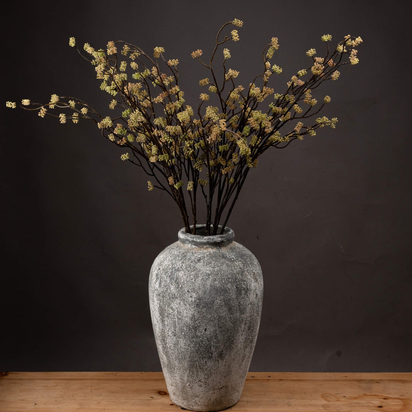 several stems in aged stone vase on wooden sideboard