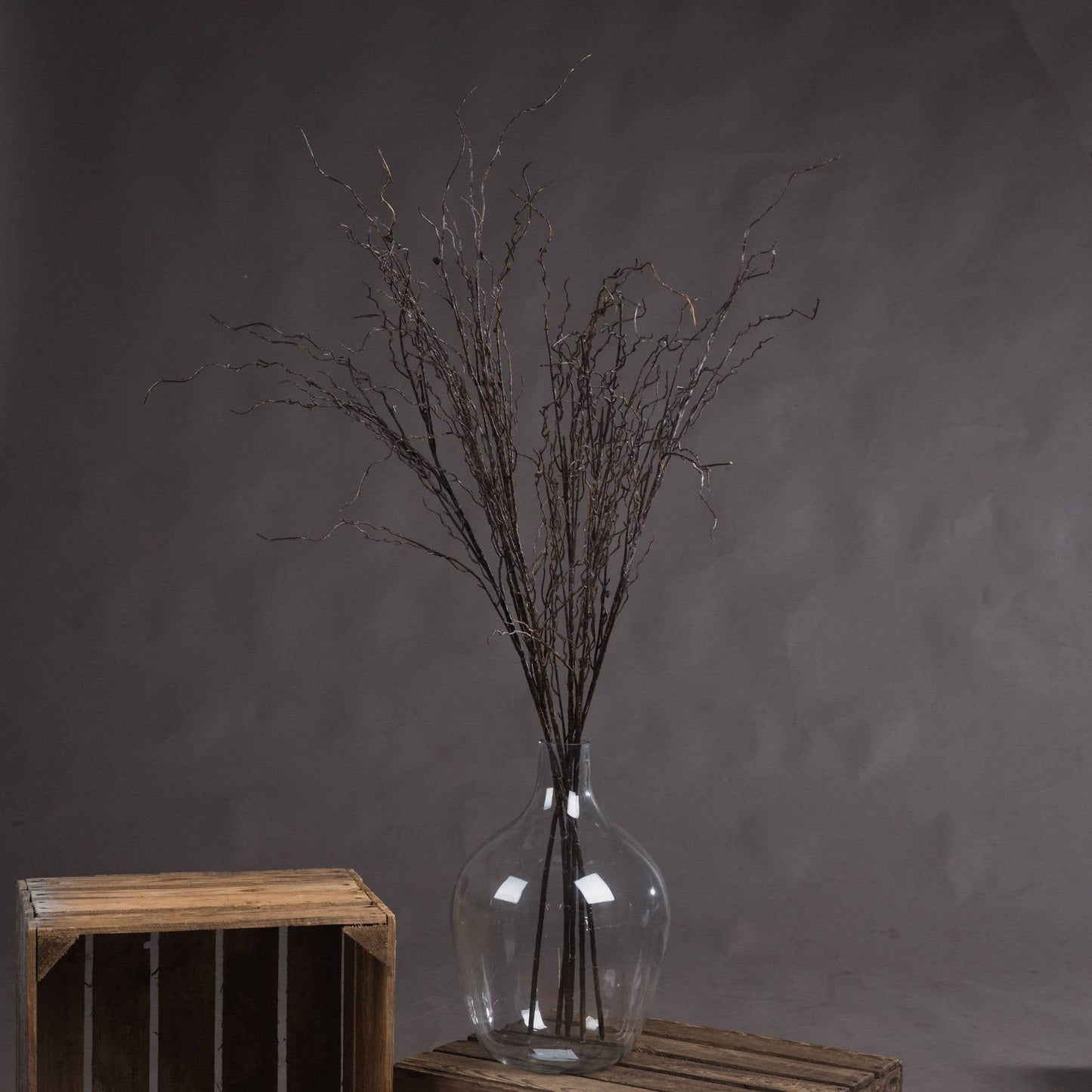 Several single stems of branch spray placed in large glass bottle neck vase on wooden crate