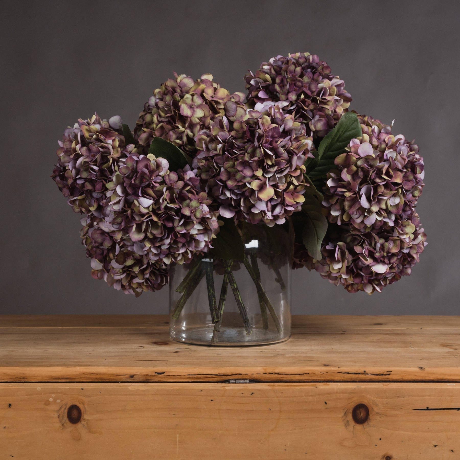 Several single stem burgundy hydrangeas in wide glass vase