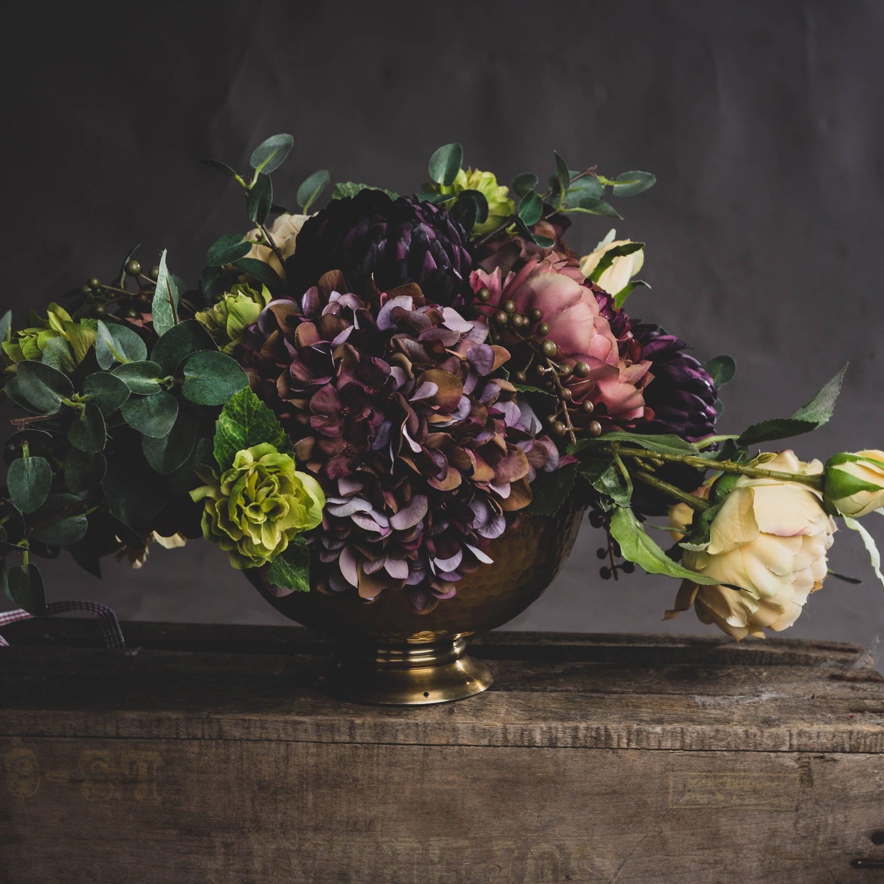 floral display comprising of burgundy hydrangea with other autumn florals in gold bucket style vase 