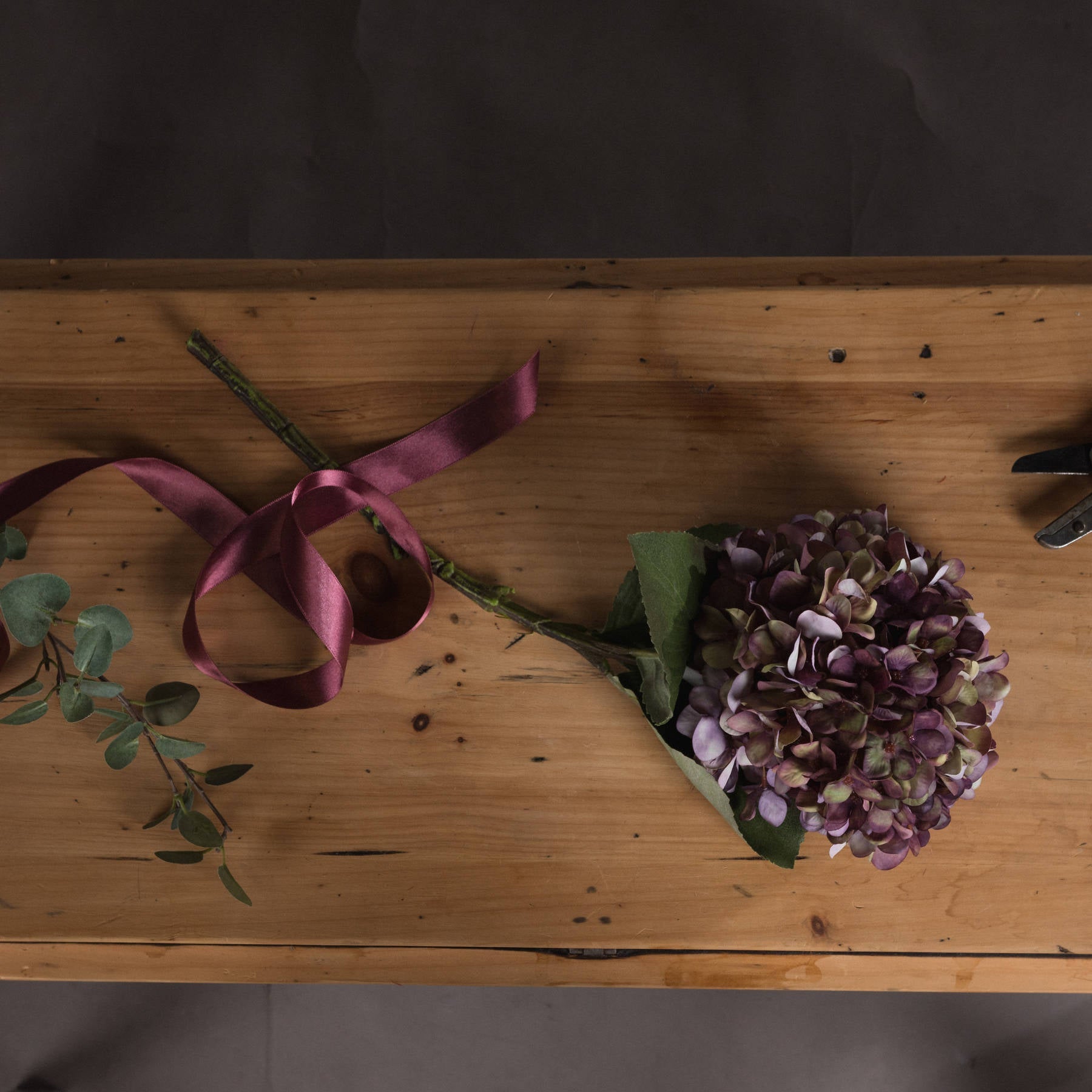 birds eye view of burgundy hydrangea laid down on sideboard with burgundy ribbon laid on the stem