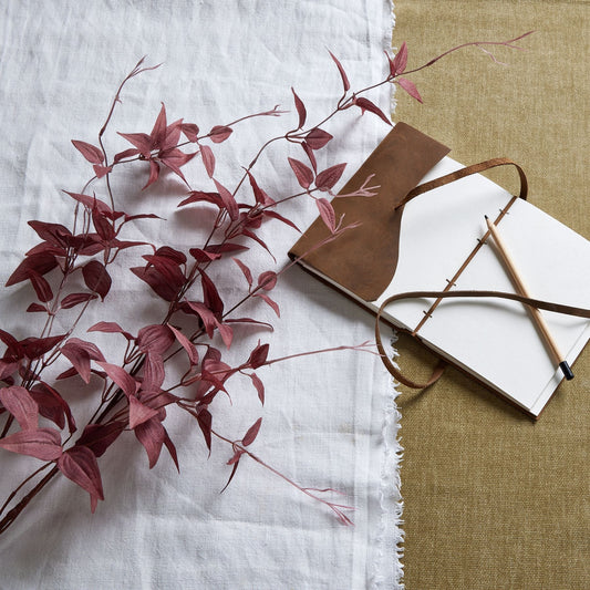 burgundy leaf stem laid down on linen next to leather bound notebook