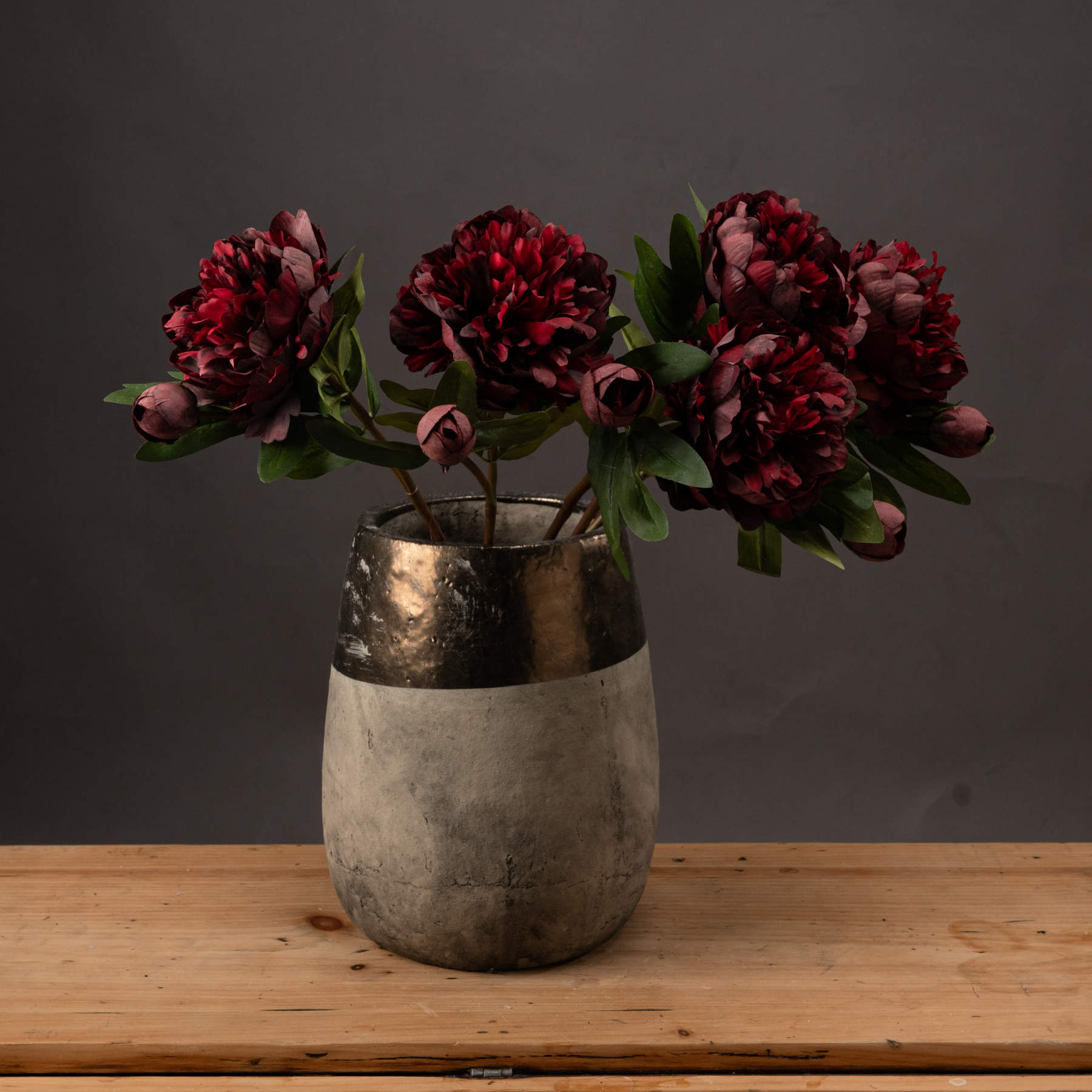 Five stems of Burgundy Peony Roses in stone vase on wooden sideboard