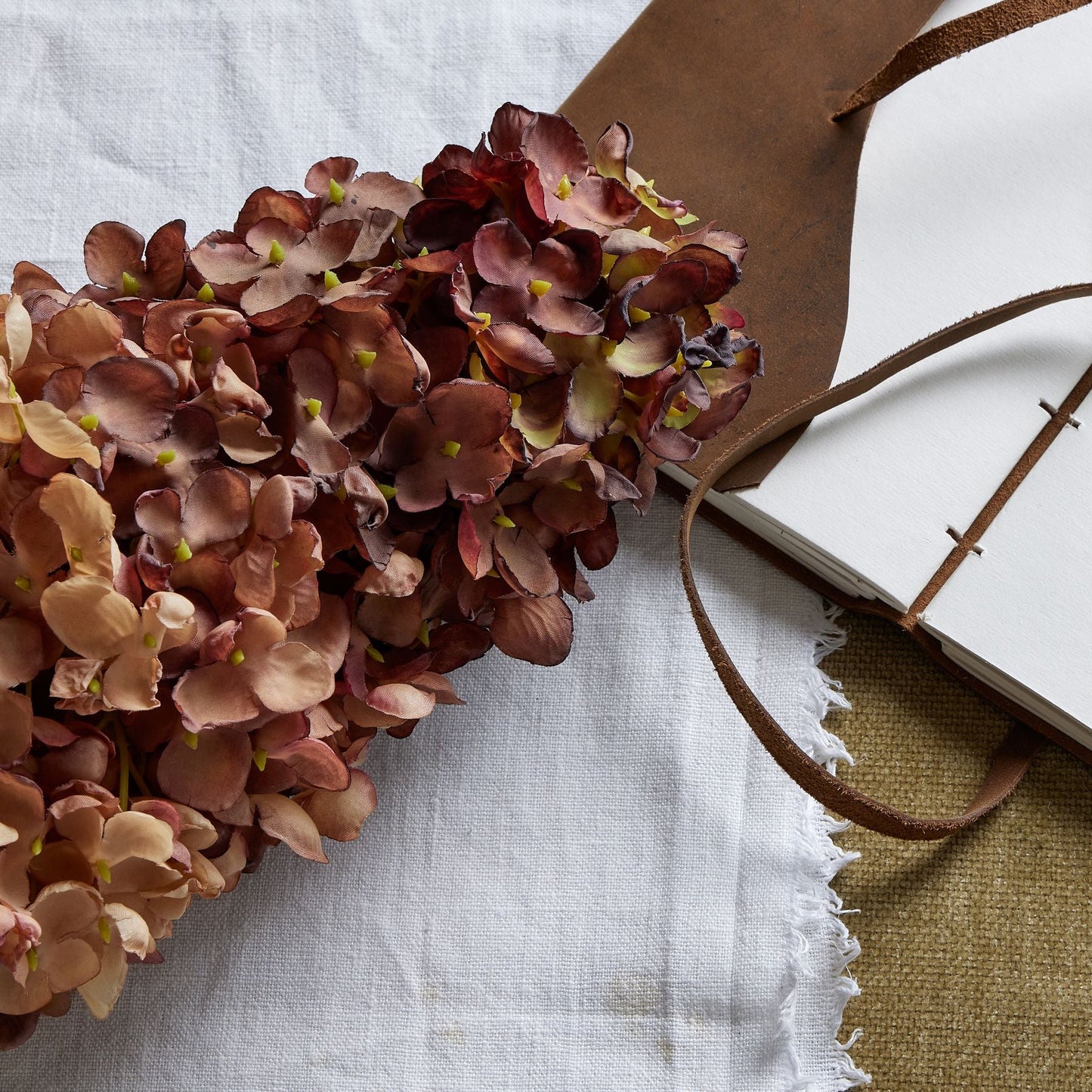 close up of the top of the spear head hydrangea laid down on white cotton and an open leather bound journal