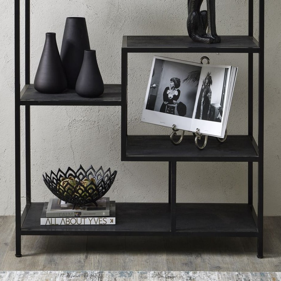 lifestyle image showing lower half of black multi shelf unit with the easel displaying a book to the right hand side, matte black vases and lattice black bowl on decorative books to the left