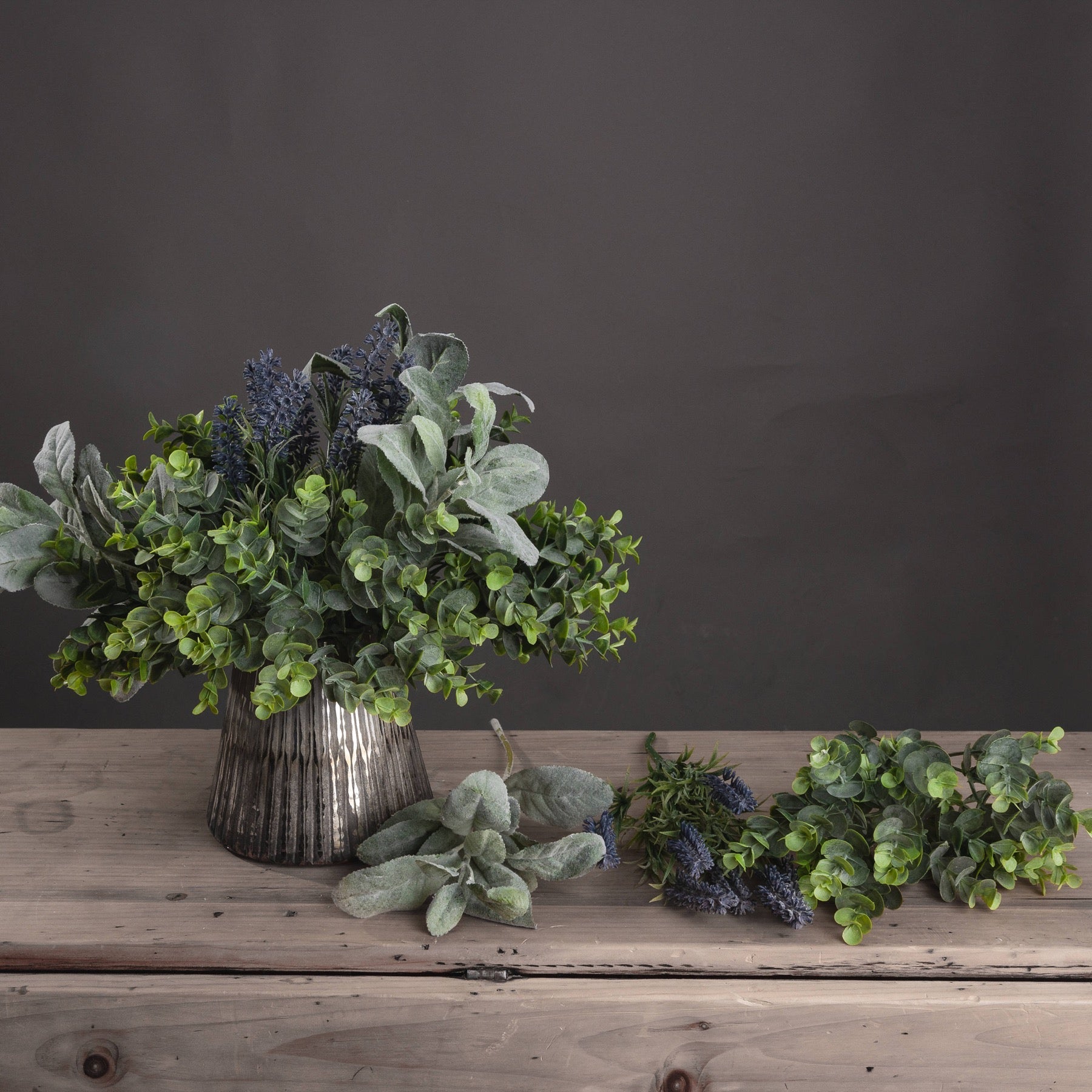 various different artificial foliage including the lambs ear spray in short silver vase in wooden sideboard