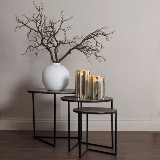 Lifestyle image of large branch spray, three stems in large globe vase on largest table of nest of three. Two candle holders are on the middle table and the smallest table is on its own