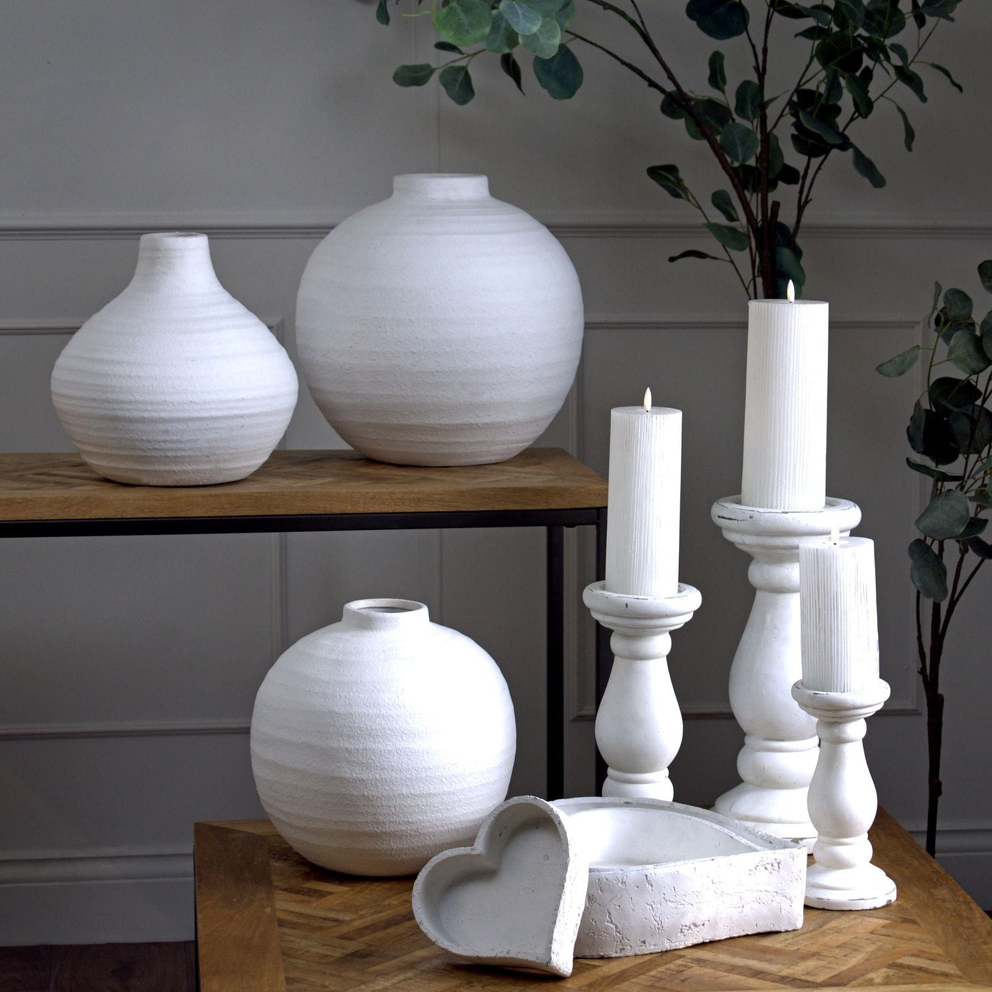 large and amphora stone vase to console table top. Small globe vase with matching candlesticks and set of three heart shaped dishes on a coffee table