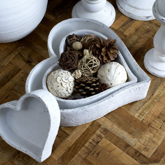 medium heart dish sat inside large dish with dried decorative balls inside, the small dish leans against the two. Placed on herringbone style table top