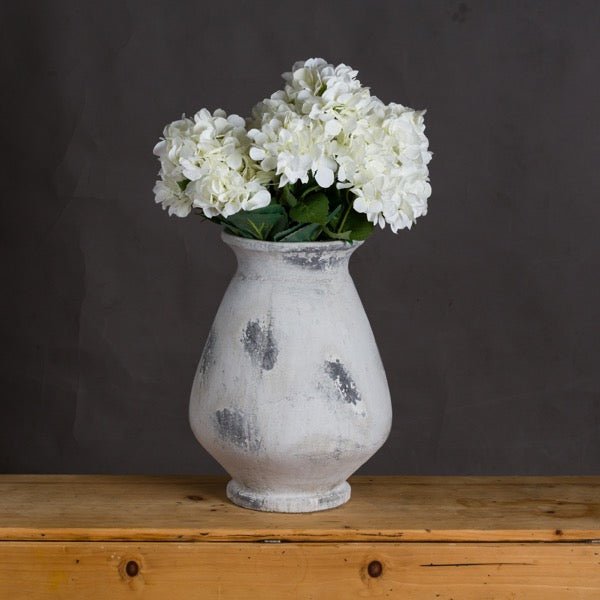 lifestyle image of the Naxos vase on wooden sideboard with white artificial flowers in