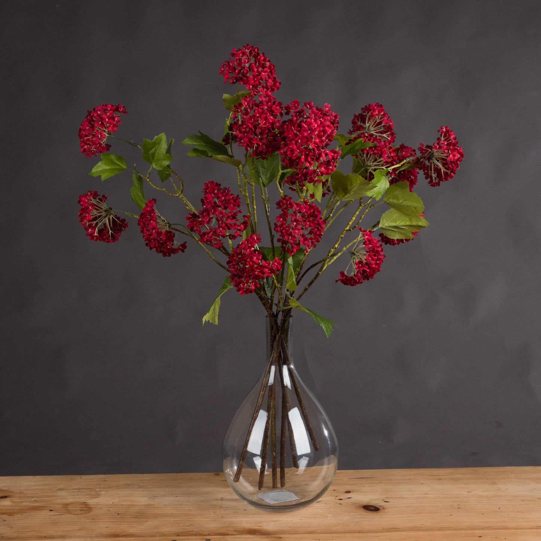 Several red viburnum stems in clear glass vase on wooden sideboard