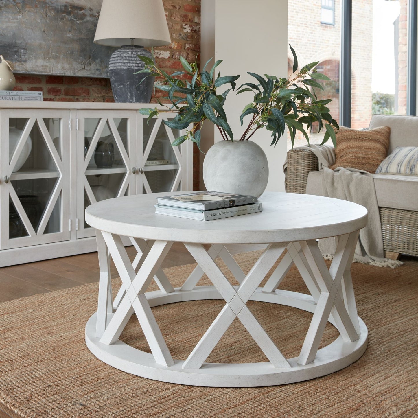 lifestyle image of the round coffee table with stone effect globe vase on top and two decorative books. A matching 4 door sideboard is in the background with a stone lamp on.