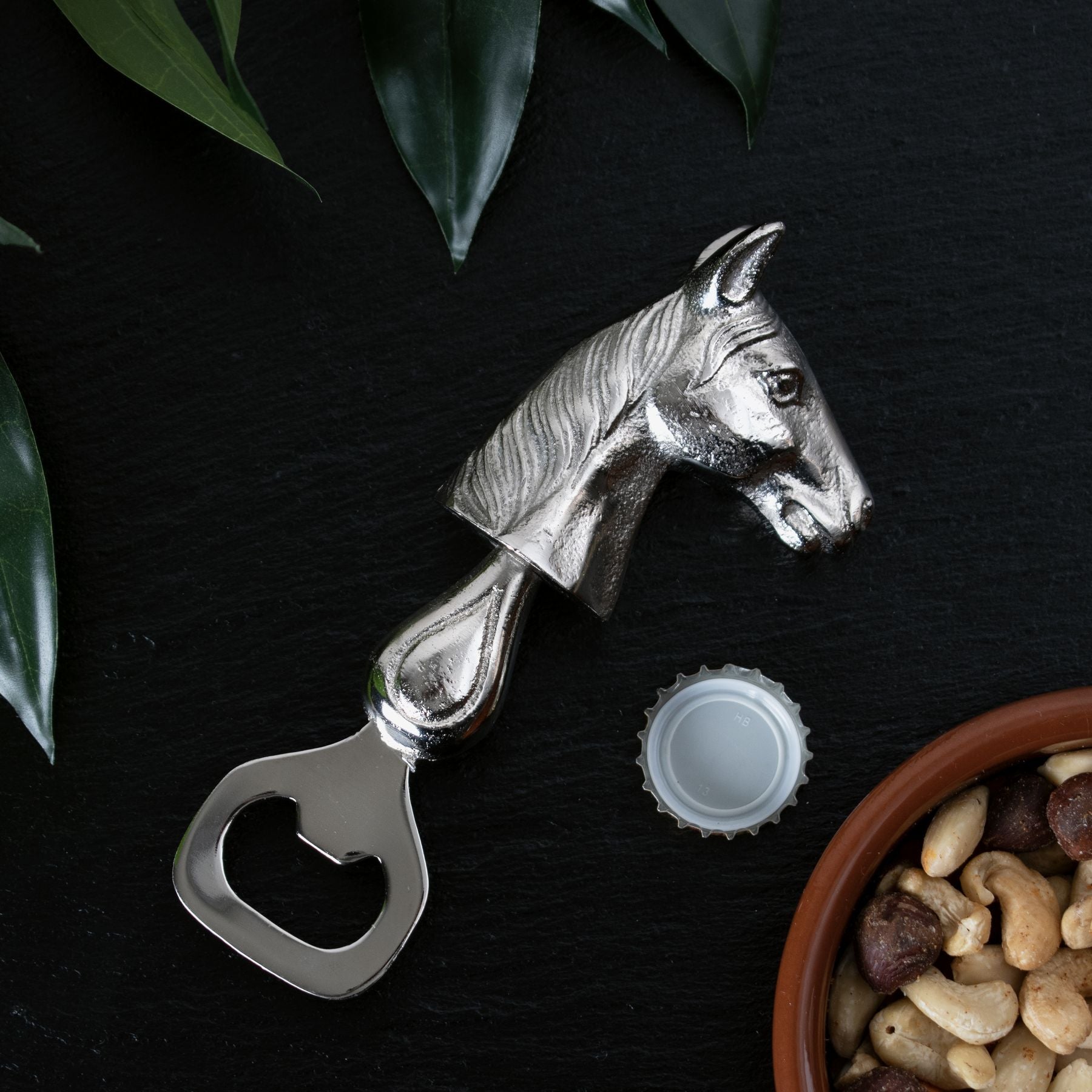 horse head bottle opener laid down next to bottle top and bowl of nuts