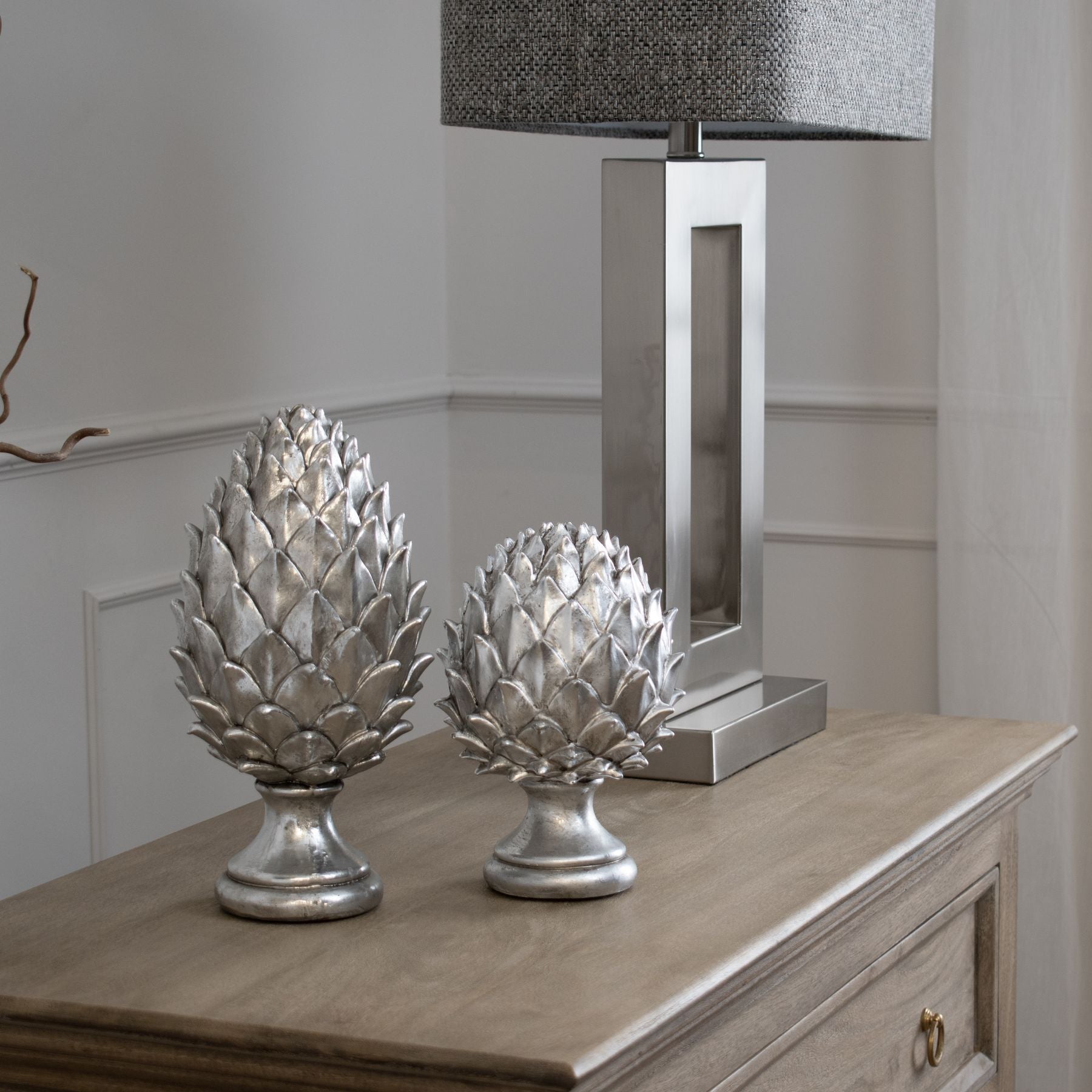 pinecone finial displayed with tall pinecone finial on sideboard next to silver lamp