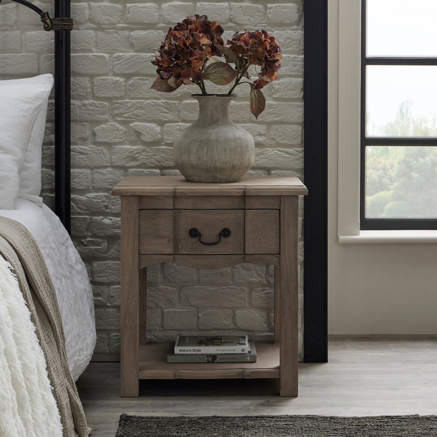 lifestyle image of squat shaped stone vase on bedside table with coffee hydrangeas in