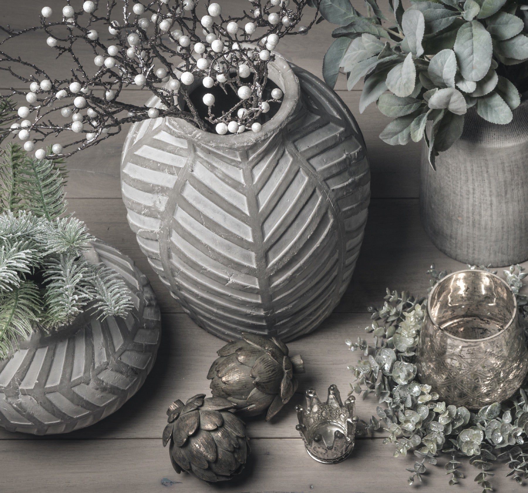 view from above the stone vase, with frosted berry branches in. Stone planter next to the vase, with bronze artichokes in front and tea light candle holders