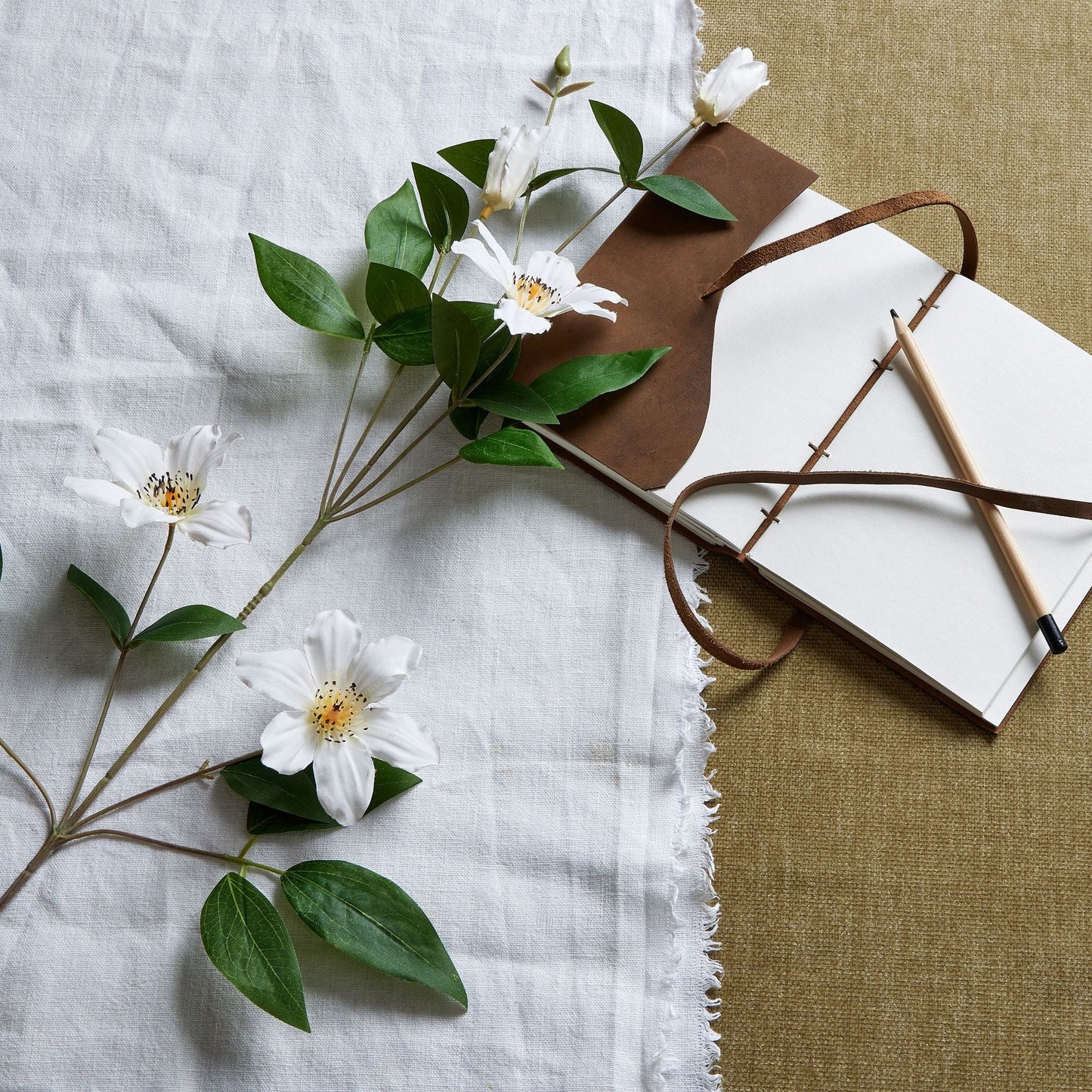 one stem of white clematis laid down next to leather bound notebook