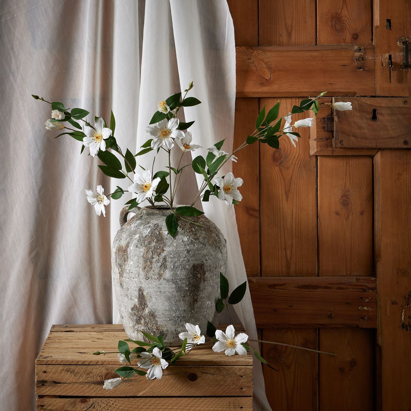 several stems of florida white clematis in an aged stone vase